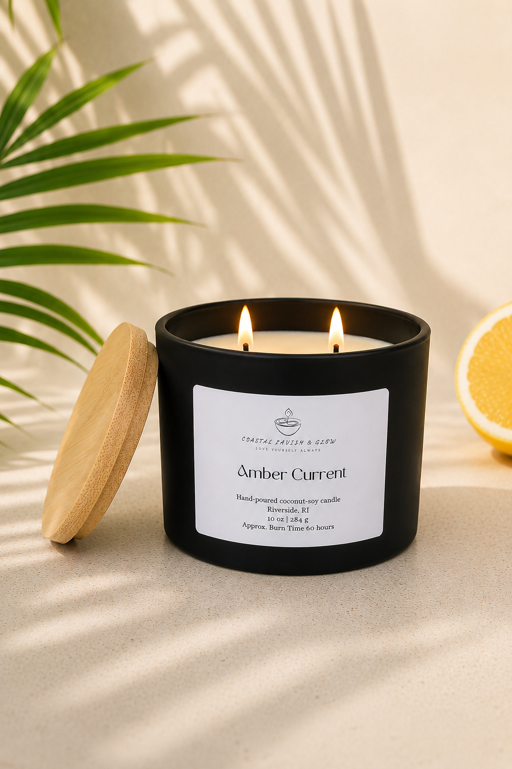 "Amber Current" black candle with a wooden lid on a beige surface, surrounded by greenery and a lemon.