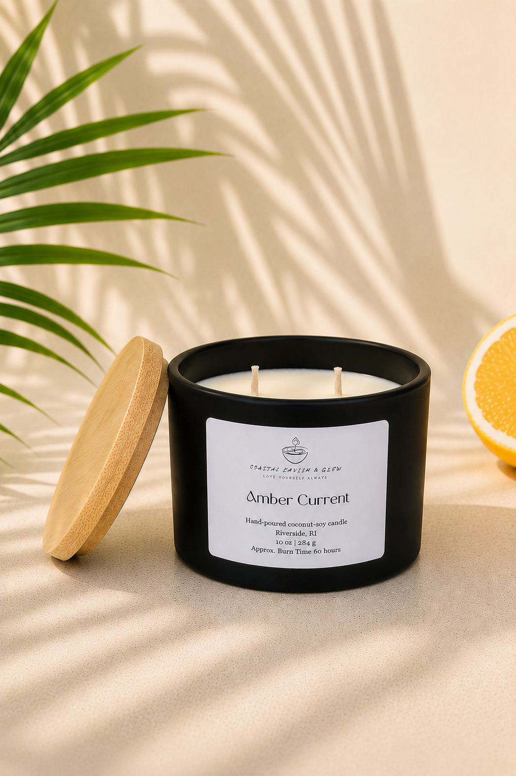 Black candle labeled 'Amber Current' with a wooden lid on a beige surface with a plant and lemon in the background.