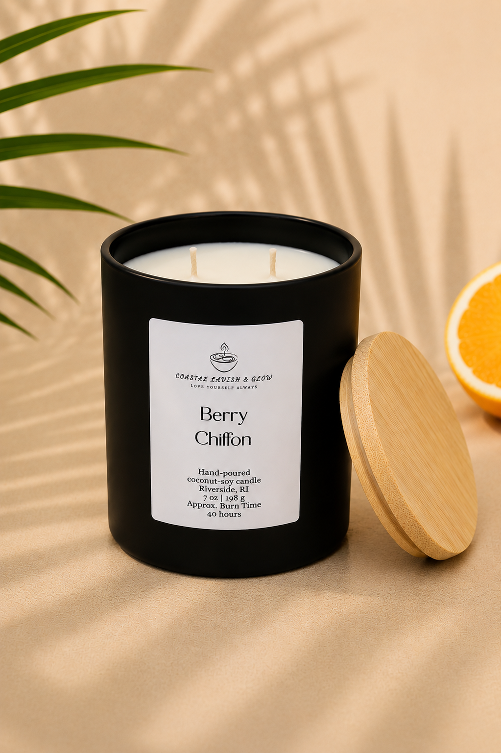 "Berry Chiffon" black candle placed on a neutral background with a plant on the side and an orange in the background
