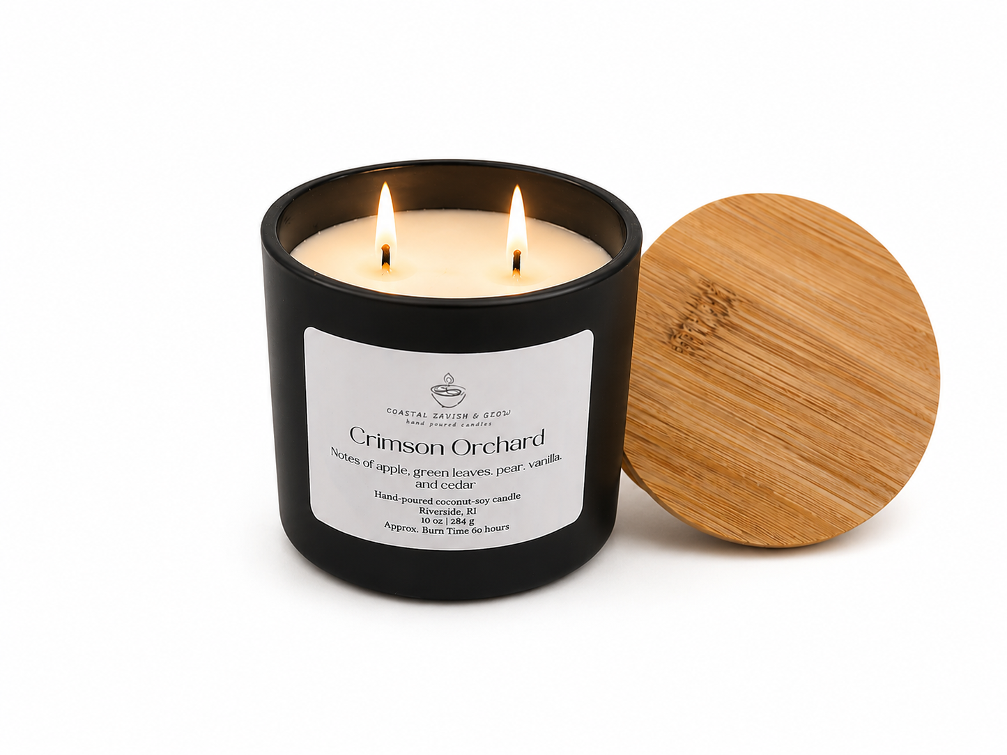 Crimson Orchard candle in a black matte vessel with two lit wicks and wooden top set to the side