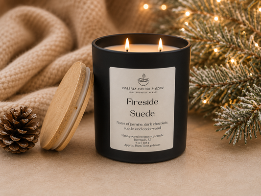 Black candle labeled 'Fireside Suede' with a wooden lid, surrounded by festive decorations on a beige surface.