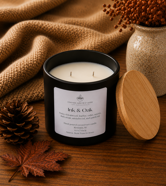 "Ink & Oak" candle with a label on a wooden surface with decorative elements like a vase, leaf, and pine cone.