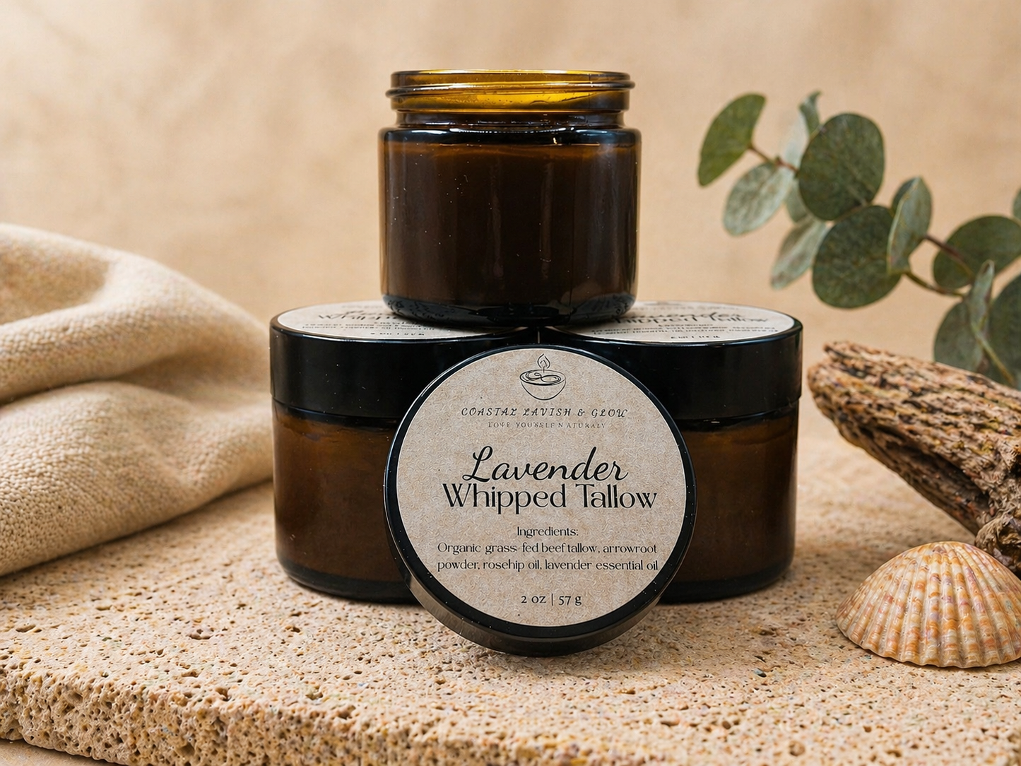 Lavender whipped tallow balm in a black container on a textured surface with eucalyptus leaves and lavender flowers.
