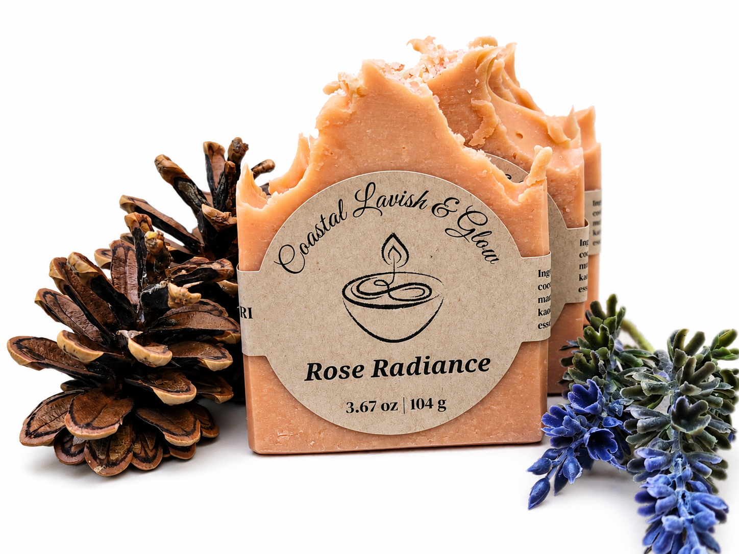 Pink bar of soap with a decorative label, surrounded by a pine cone and lavender flowers on a white background.  