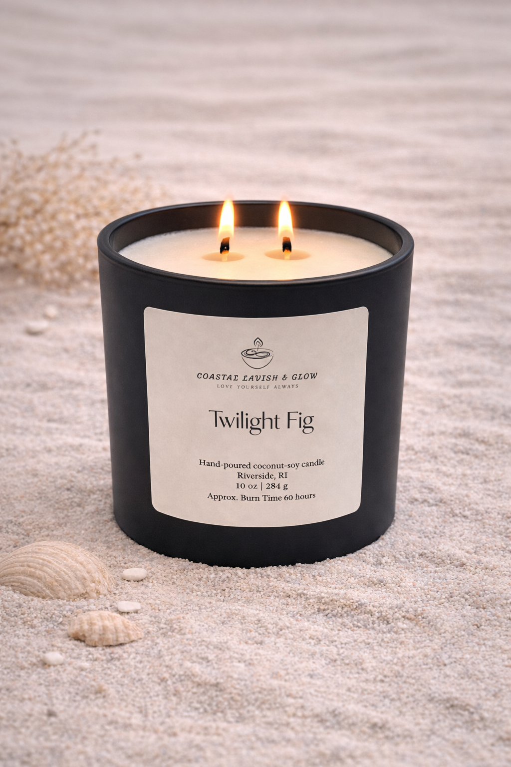 Twilight Fig candle in a black container on sand with seashells - citrus, plum, black cherry, amber scent
