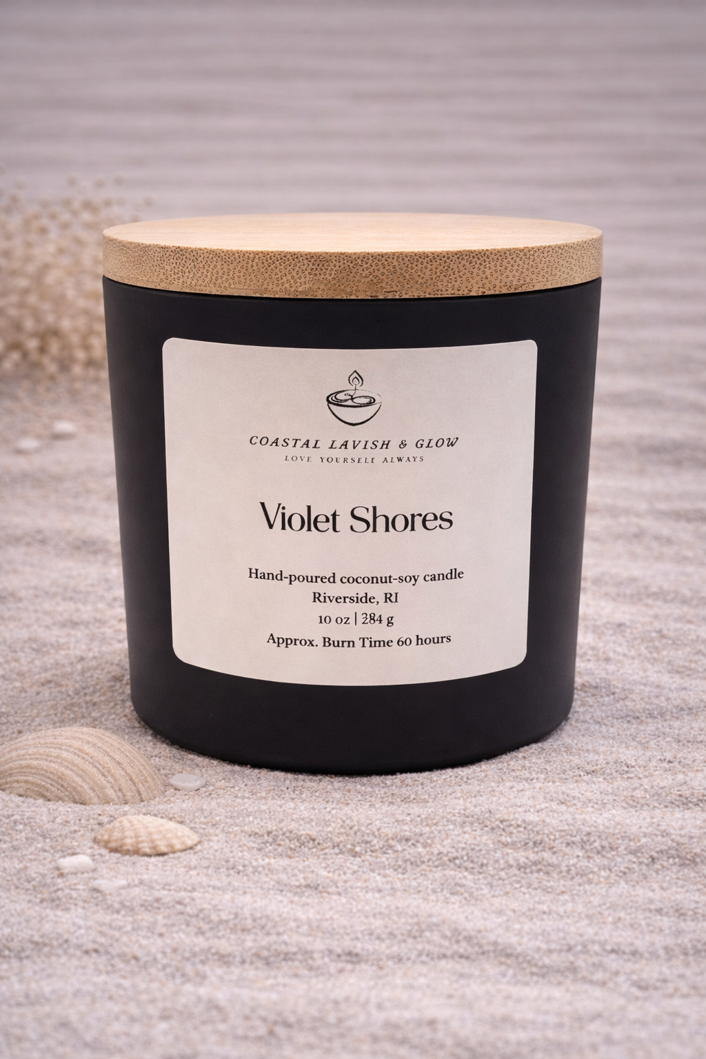 Violet Shores black glass candle with a wooden lid on a beachy surface.  Lavender and sage scent.