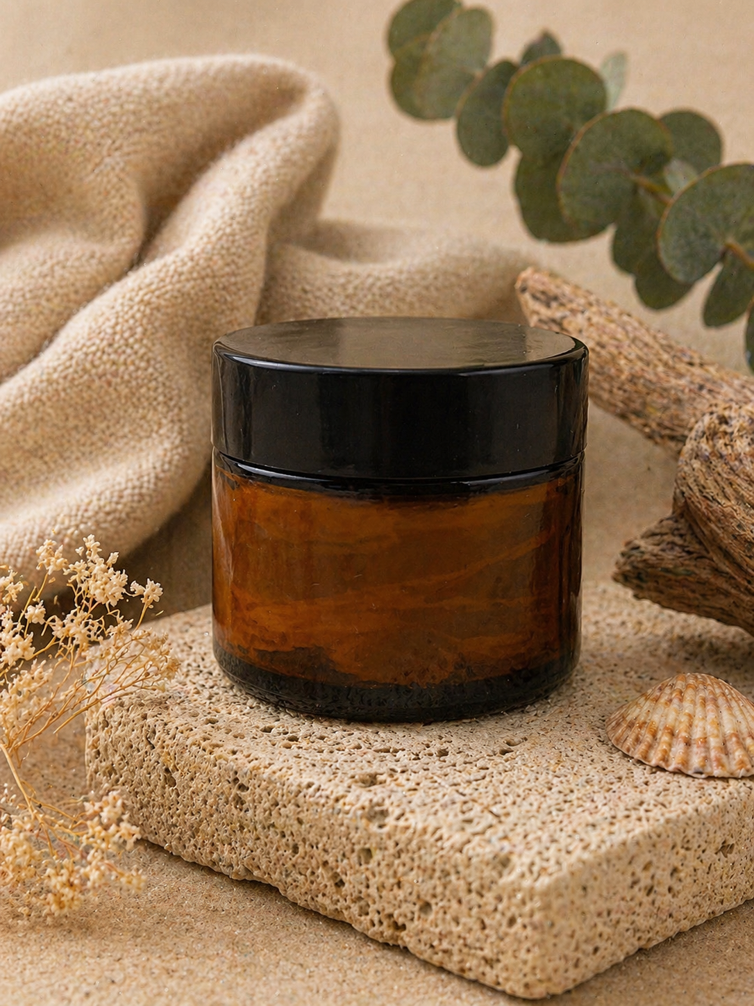 Sandalwood scented whipped tallow in a brown glass jar with black lid on a textured surface with beige towel and eucalyptus leaves in the background